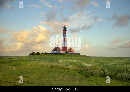 Weißer und orangener Leuchtturm auf einem Feld, umgeben von Bäumen Stockfoto