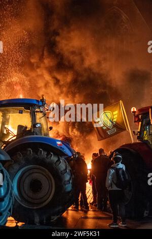 Turnhout, Antwerpen, Belgien, 28. Januar 2024, das Bild fängt einen dynamischen und intensiven Moment während des Protests der Landwirte gegen das Stickstoffabkommen in Turnhout, Belgien, ein. Eine Gruppe von Demonstranten wird in dicken Rauchwolken gesehen, mit dem feurigen Schein eines Lagerfeuers, das die Szene beleuchtet. Ein Traktor, symbolisch für die landwirtschaftliche Gemeinschaft, steht im Vordergrund, während die Demonstranten Fahnen tragen, die ihre Solidarität und ihren Zweck bezeugen. Die nächtliche Umgebung, kombiniert mit der dramatischen Beleuchtung des Feuers, vermittelt die Dringlichkeit und die aufgeheizten Emotionen der Veranstaltung. Landwirte Stockfoto