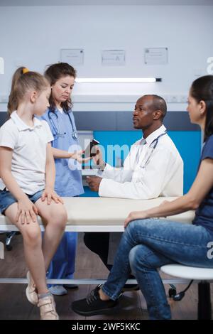 Arzt gibt verschreibungspflichtige Pillen Flasche zu Hilfe Krankenschwester in der medizinischen Praxis. Kaukasische Mutter mit jungem Mädchen im Gesundheitsamt, Behandlung von Kinderarzt, Beratung über Medikamente. Stockfoto