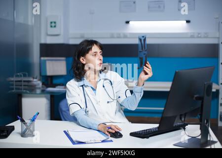 Ein spezieller Arzt untersucht einen CT-Scan eines Patienten und macht sich Notizen auf dem Desktop-Computer. Das Bild zeigt eine kaukasische Ärztin, die ein Thorax-Röntgenbild einer Person inspiziert. Stockfoto
