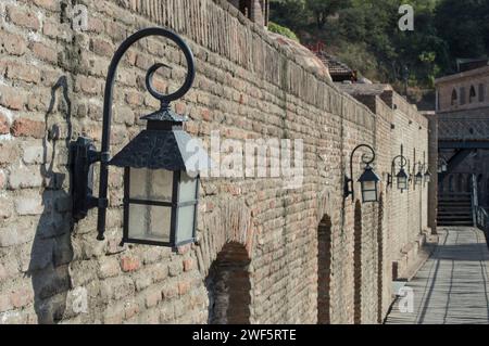 Eine Reihe von Vintage-Straßenlaternen wirft sanfte Schatten auf eine alte Ziegelwand und zeigt den Charme und die Geschichte der alten Welt in einer ruhigen Umgebung. Stockfoto