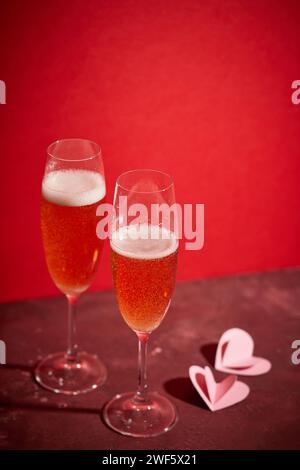 Zwei Gläser Champagner und herzförmige Dekorationen auf rotem Hintergrund Stockfoto