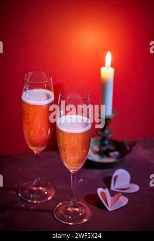 Zwei Gläser Champagner und eine brennende Kerze auf rotem Hintergrund Stockfoto