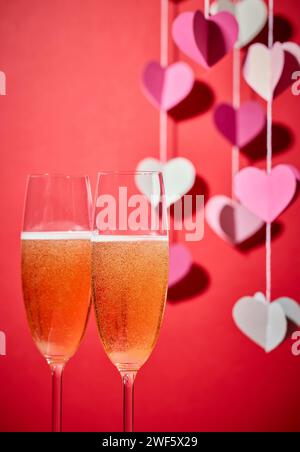 Zwei Gläser Champagner und defokussierte herzförmige Dekoration auf rotem Hintergrund Stockfoto