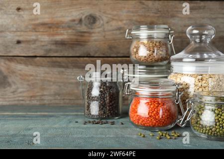 Verschiedene Arten von Hülsenfrüchten und Getreide in Glasgefäßen auf einem blauen Holztisch, Platz für Text. Organische Körner Stockfoto