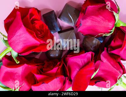 Köstliche Schokoladenbonbons und rote Rosen auf rosa Hintergrund, Aquarelleffekt. Stockfoto