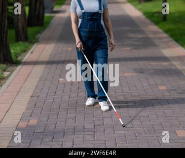 Eine gesichtslose blinde schwangere Frau läuft mit einem Stock die Straße entlang. Stockfoto