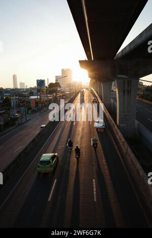 Bangkok, Thailand - 24. November 2023: Silhouettenszene des morgendlichen Transports auf der Hauptstraße unter der Skytrain-Eisenbahn in Bangkok, Thailand mit Gold Stockfoto