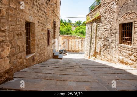 Gubbio Umbria, Italien,- 14. Mai 2011; Person auf Moped verschwimmt in Bewegung am Ende der kurzen italienischen Steinstraße an der sonnigen Kreuzung Stockfoto
