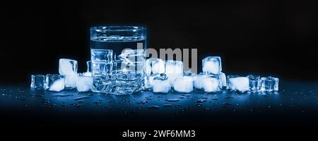 Gekühltes sauberes Wasser in einem Glas vor einem Hintergrund aus Eiswürfeln, auf dunklem Hintergrund Stockfoto