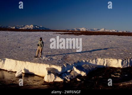 Person, die während des Frühlingsaufbruchs auf Eis steht, nördlich der Brooks Range, mit dem Arctic National Wildlife Refuge im Hintergrund, Alaska Stockfoto