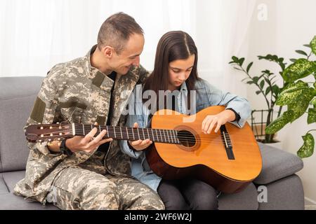 Der Veteran kam aus der Armee zurück. Ein Mann in Uniform mit seiner Tochter. Der Veteran spielt Gitarre. Stockfoto