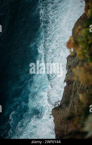 Ein Blick aus der Luft auf turbulente Meereswellen, die gegen felsiges Ufer krachen. Stockfoto