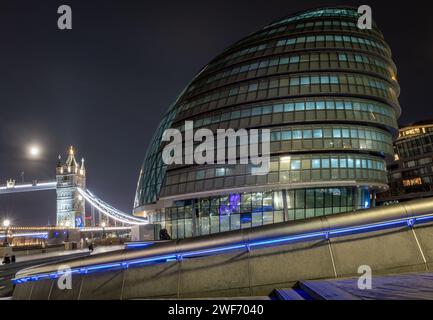 London. UK-01.27.2024. Nächtlicher Blick auf das Rathaus mit der Tower Bridge im Hintergrund. Büro- und Verwaltungsgebäude des Londoner Bürgermeisters. Stockfoto