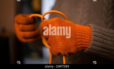 Die Hand eines Mannes in orangefarbenen Arbeitshandschuhen löst den orangefarbenen Draht Stockfoto