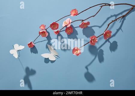 Ansicht von oben auf rosa Papierblumen Zweig und weiße Schmetterlinge auf blauem Hintergrund. Rahmen mit Pfirsichblüte. Hintergrund für Werbung. Dekoration für n Stockfoto