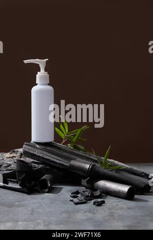 Leerer Kosmetikbehälter aus Kunststoff für Creme oder Shampoo auf braunem Hintergrund. Kosmetikflaschenmockup kombiniert mit Stein-, Blatt- und Bambuskohle. Bea Stockfoto