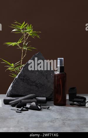 Vorderansicht von grauen Steinen, grünen Blättern und Bambuskohle auf braunem Hintergrund. Mockup für Design, Bio-Kosmetik, Kosmetikkonzept für Kosmetikprodukte. Stockfoto