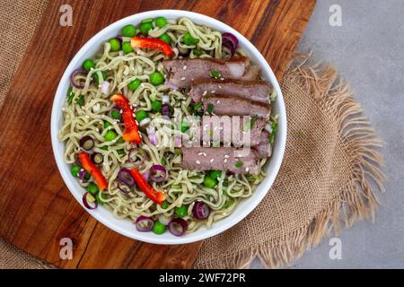 Spinat und Grünkohl Ramen-Nudeln mit Frühlingszwiebeln, Erbsen und Rindfleisch in Scheiben, Blick von oben. Flache Lage mit rustikalem Holz und Sackleinen mit Kopierraum Stockfoto