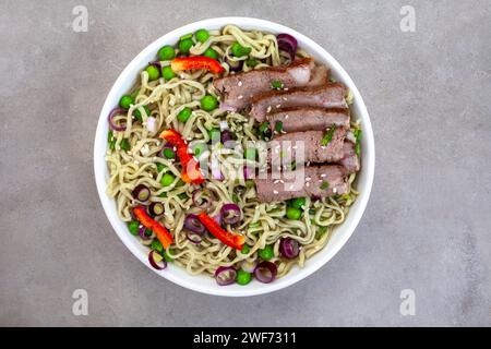 Spinat und Grünkohl Ramen-Nudeln mit Frühlingszwiebeln, Erbsen und Rinderscheiben auf grau meliertem Rindfleisch mit Kopierraum Stockfoto