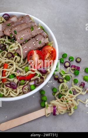 Spinat und Grünkohl Ramen-Nudeln mit Frühlingszwiebeln, Erbsen und Rinderscheiben auf grau meliertem Rindfleisch mit Kopierraum Stockfoto