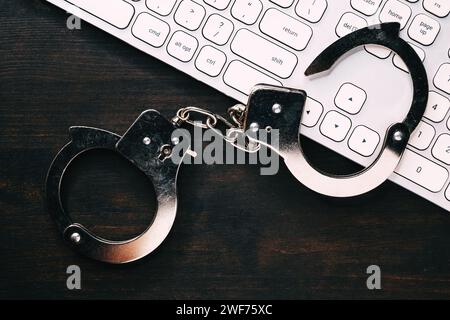 High-Tech-IT-Konzept zur Verhaftung von Cyberkriminalität, Bild von Polizeihandschellen über Computertastatur, selektiver Fokus Stockfoto
