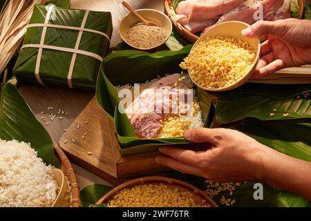 Hände, die Mungbohnen in eine mit Dong-Blättern gefütterte Schachtel geben, wenn sie klebrigen Reiskuchen machen. Hintergrund für Urlaubskost-Werbung, Draufsicht Stockfoto