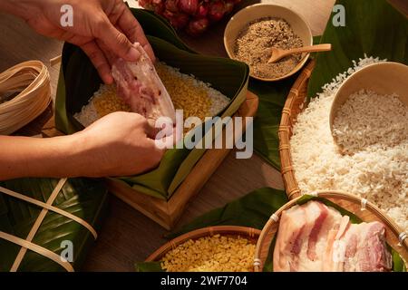 Hände, die fettes Schweinefleisch in eine mit Dong-Blättern gefütterte Schachtel geben, wenn sie einen klebrigen Reiskuchen (Chung-Kuchen) machen. Traditionelles Mondneujahrsessen. Konzept für Werbung Stockfoto