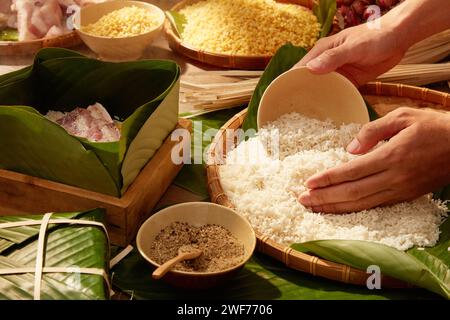 Hände legen weißen Reis in eine Box, die mit Dong-Blättern ausgesäumt ist, wenn sie klebrigen Reiskuchen (Chung-Kuchen) machen. Traditionelles Mondneujahrsessen Stockfoto