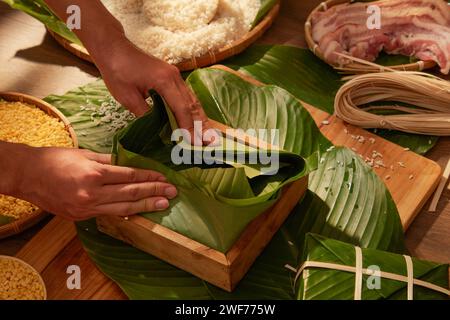 Vorderansicht des Küchenchefs, der Chung-Kuchen (klebriger Reiskuchen) mit Schweinefleisch und Mais im Hintergrund der Holzküche herstellt. Chinesisches Neujahrsfest Stockfoto