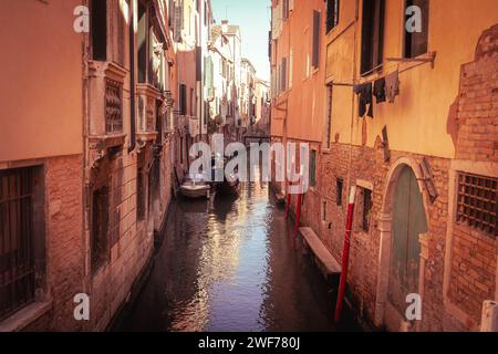 Werfen Sie einen Blick in das lokale Leben, während ein Gondoliere in der Abenddämmerung durch die engen Kanäle eines Wohnviertels in Venedig navigiert. Stockfoto