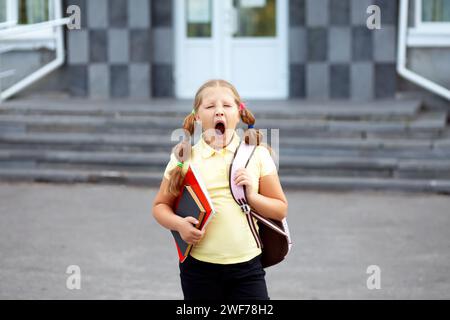 Hübsches Schulmädchen, das nach dem Unterricht vor der Tür der Schule gähnt. Müde Schülerin - harter Schultag Stockfoto