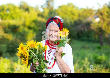 Gelb blaues Herz und ein Blumenstrauß in den Händen einer alten Großmutter in einem gestickten Hemd und roten Perlen. Unabhängigkeitstag des vereinigten königreichs Stockfoto