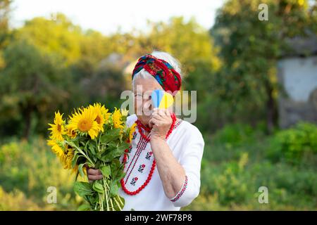 Gelb blaues Herz und ein Blumenstrauß in den Händen einer alten Großmutter in einem gestickten Hemd und roten Perlen. Unabhängigkeitstag des vereinigten königreichs Stockfoto