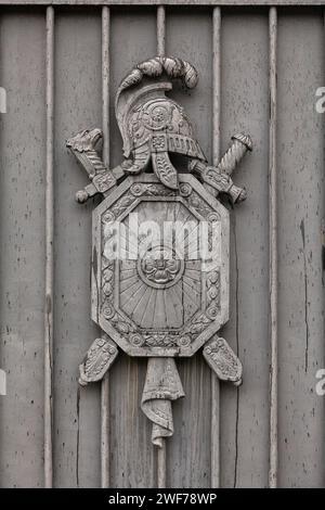 Ein altes Wappen in Form eines Schildes, zwei gekreuzte Schwerter und ein Helm an einem alten Tor. Stockfoto