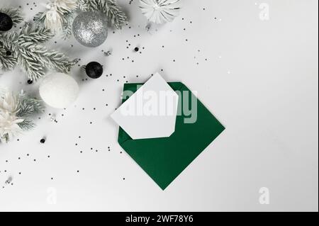 Weihnachtskomposition, grüner Umschlag, weiße und silberne Dekorationen, Tannenzweige, silberne Sterne Konfetti auf weißem Hintergrund. Stockfoto