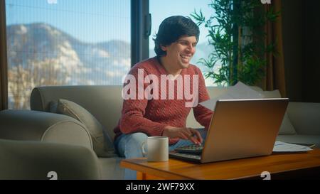 Überfröhlicher junger Mann sitzt auf der Couch im Wohnzimmer mit Laptop Rechnungen bezahlen, Taschenrechner Zählkosten verwenden, Budget kontrollieren, Finanzen verwalten Stockfoto