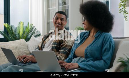 Afroamerikanerin arbeitet mit Laptop Mann Computer arbeitendes Paar sitzen in Reihe zwei Freiberufler mit Computern kooperieren zu Hause süchtig Familie sucht sucht Stockfoto