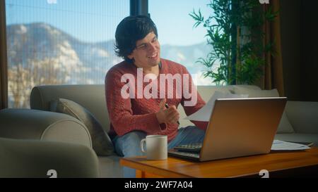 Junger Mann sitzt auf der Couch im Wohnzimmer mit Laptop, bezahlt Rechnungen, verwendet Taschenrechner Zählkosten, führt Budgetkontrolle durch, verwaltet Finanzen Stockfoto