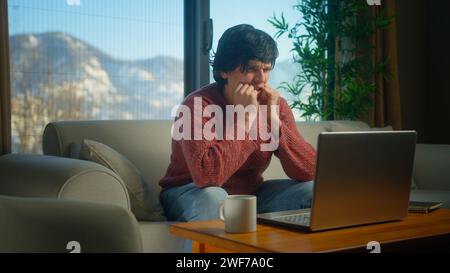 Junger Mann sitzt auf dem Sofa, leidet an Brustschmerzen, hat einen Herzinfarkt, hält die Brust massierend, während er mit dem Laptop arbeitet. Männliche Atembeschwerden Schlaganfall bei h Stockfoto