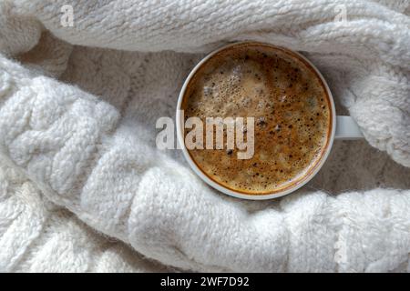 Eine Tasse schwarzen Kaffees, verpackt in einen milchigen Wollstrick-Pullover Stockfoto