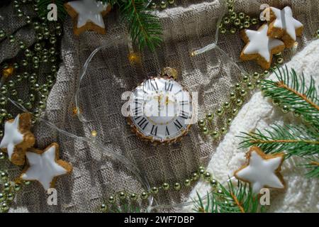 Weihnachtsbaumspielzeug in Form einer Uhr zwischen den Zweigen eines Weihnachtsbaums und Weihnachtsdekorationen Stockfoto