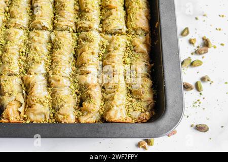 Nahaufnahme der gerollten Baklava in einer Backform auf einer weißen Oberfläche Stockfoto