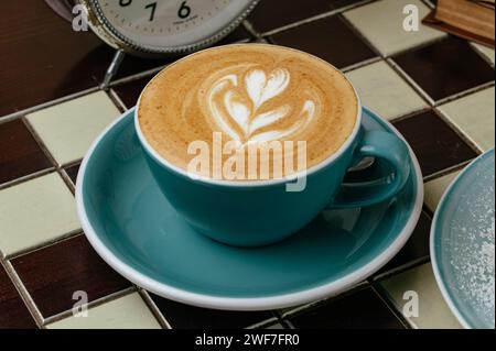 Kaffee in einer Tasse auf dem Tisch. Uhren und Bücher liegen als Nächstes Stockfoto