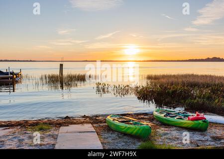 Ruhiger Sonnenaufgang am See mit Kajaks am Strand bereit für Abenteuer Stockfoto