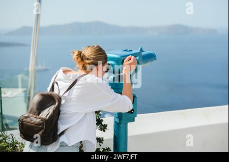 Die junge Frau schaut durch das Fernglas des Turms an der Küste von Santorin Stockfoto