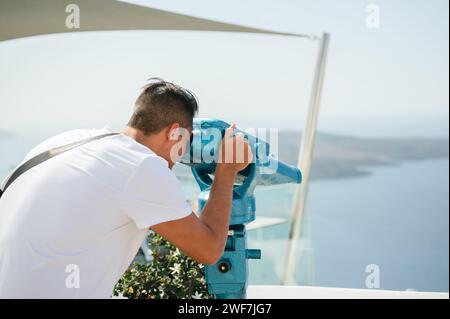 Mann, der durch das Fernglas des Turms auf die Küste von Santorin blickt Stockfoto