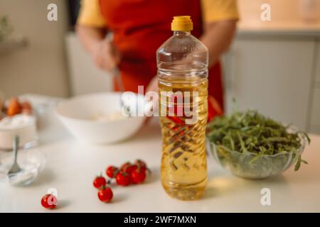 Weibliche Chefin in einer Uniform gießt Olivenöl aus einer Flasche. Kaukasische Bloggerin, die erklärt, wie man ein Gericht kocht Stockfoto