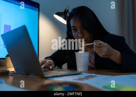 Eine Büroangestellte, die spät arbeitet und Instant-Nudeln alleine im Büro isst Stockfoto