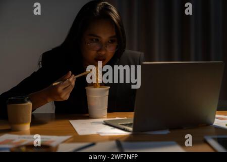 Eine Büroangestellte, die spät arbeitet und Instant-Nudeln alleine im Büro isst Stockfoto